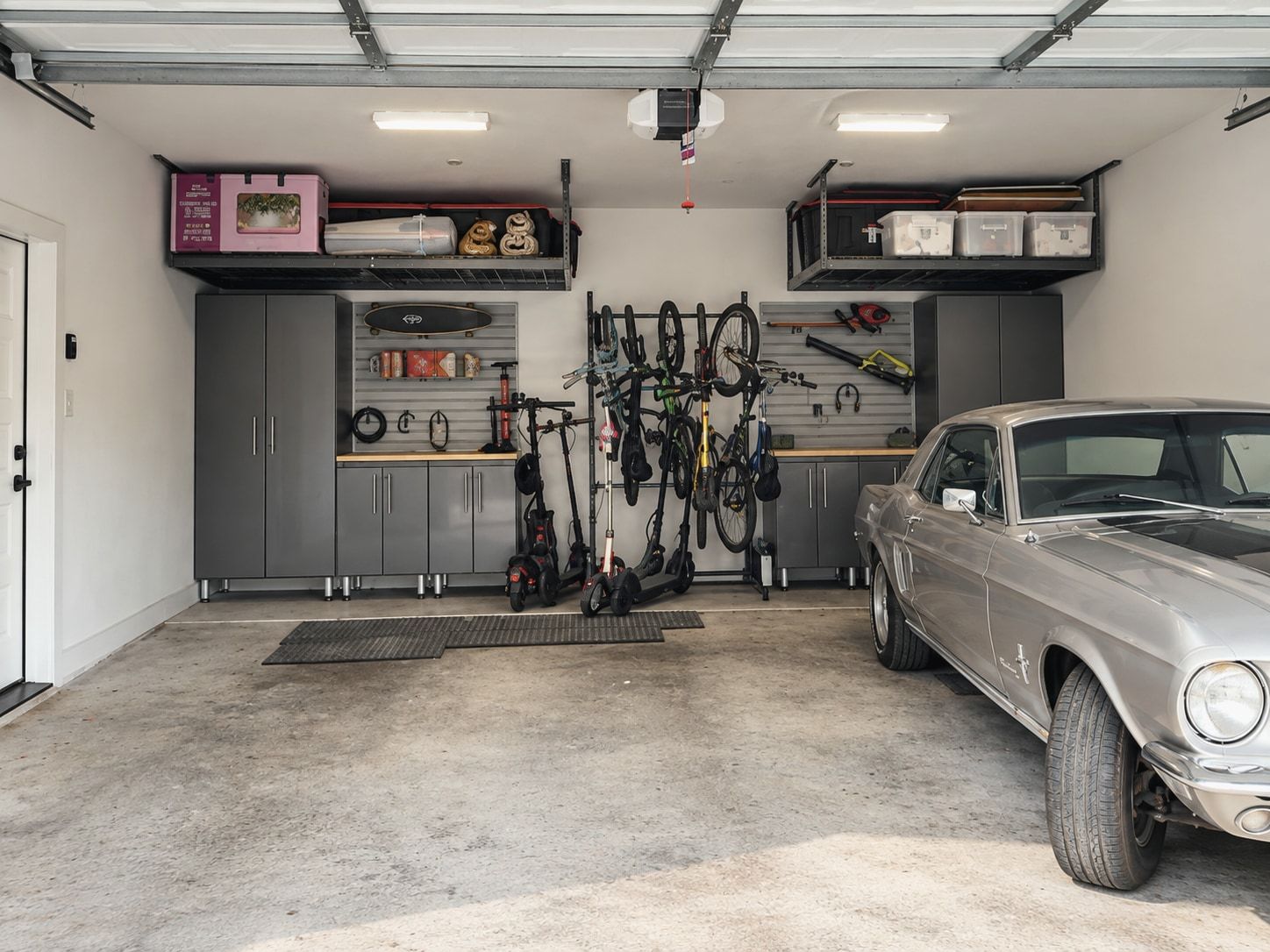 Garage after: grey cabinetry, a wall system holding bikes and tools, overhead racks, and the car parked inside
